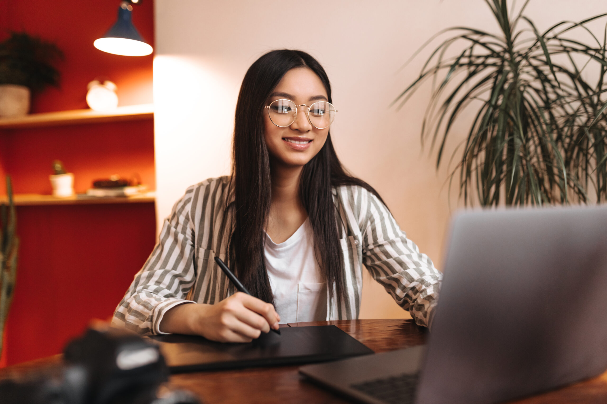 smiling woman employee striped outfit glasses looks into laptop holds pen scaled